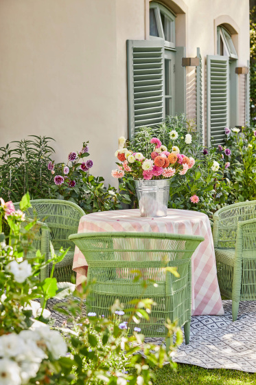Outside dining area with three bright green garden chairs and a warm neutral wall (Clay) surrounded by flowers and greenery.
