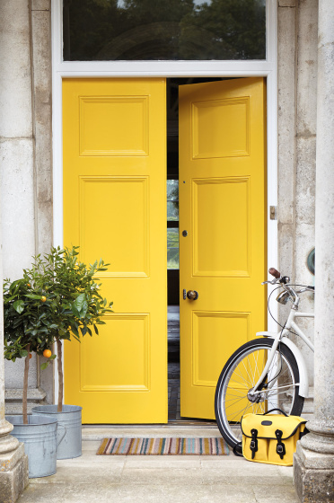 Front door painted in bright yellow 'Mister David' with two trees and a bike under pillars.