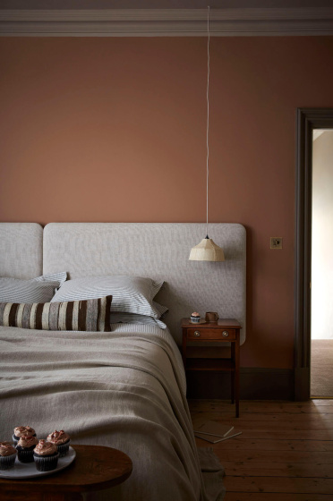 Bedroom painted in muted pink shade 'Split Pink' with a double bed next to a wooden sidetable.