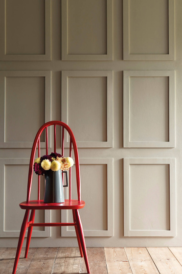 Paneled wall painted in neutral shade 'Portland Stone - Dark' with a bright red chair in front with a vase of flowers on top.
