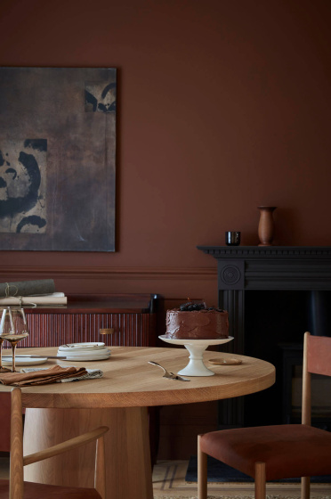 Dining space colour drenched in deep brown shade 'Ganache' with a wooden table and chairs under abstract wall art.