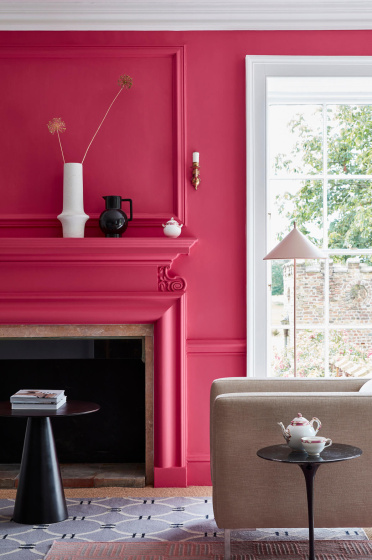 Living space painted in bright pink 'Leather' with a matching fireplace and  contrasting white window frame and an armchair.