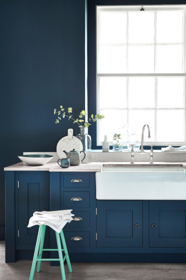 Kitchen painted in dark blue (Hicks' Blue) with a contrasting bright green (Green Verditer) stool underneath a window.