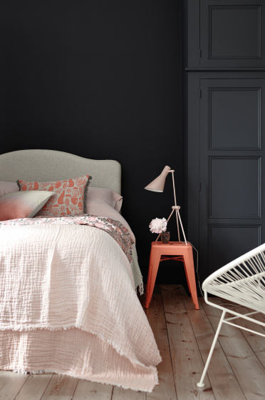 Bedroom painted in blue black 'Basalt' with a light pink bed and a contrasting bright orange stool.