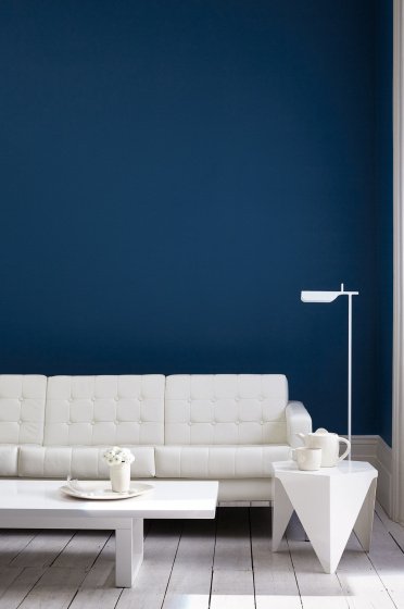 Living room painted in dark blue (Royal Navy) with a white sofa, lamp, table and wooden floor.