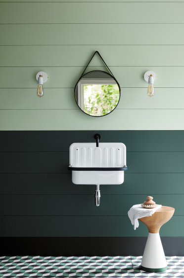 Paneled bathroom with the upper wall painted in Aquamarine and lower wall in dark green with a white sink and round mirror.