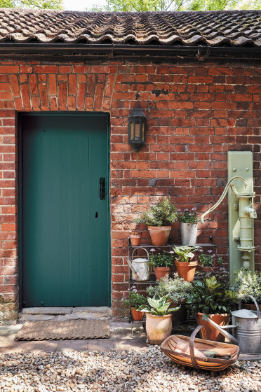 Brick exterior with a dark green (Goblin) door with several potted plants and a pebbled floor.