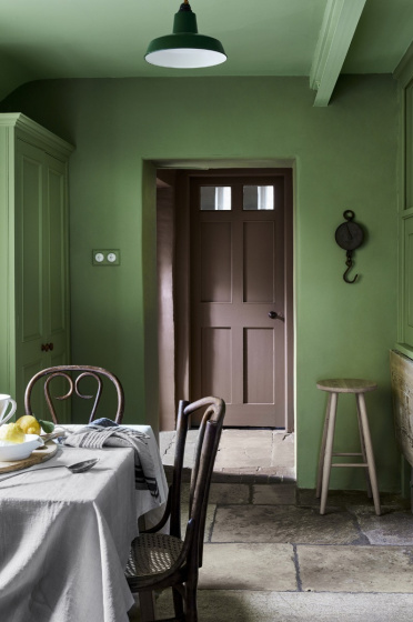 Deep green (Garden) dining space with contrasting brown door and a dining room table with chairs.