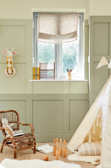 Children's nursery painted in 3 different shades of green neutral 'Green Stone' with children's toys and a small wicker chair.
