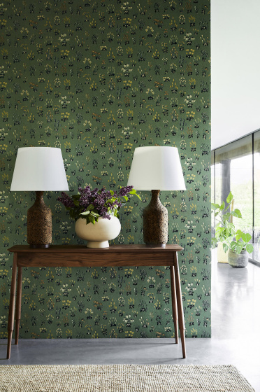 Hallway with green small floral wallpaper 'Millefleur - Garden' and a wooden sidetable with 2 lamps and a vase of flowers.