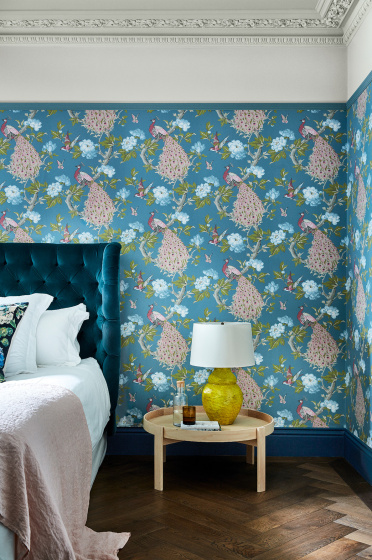 Bedroom with a blue bird print wallpaper (Pavona - Sylvie) and a small wooden table next to the bed.