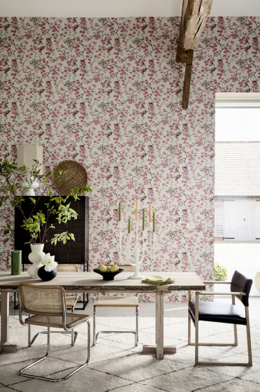 Dining room with pink printed floral and bird wallpaper (Massingberd Blossom - Mineral) and wooden dining table and chairs.