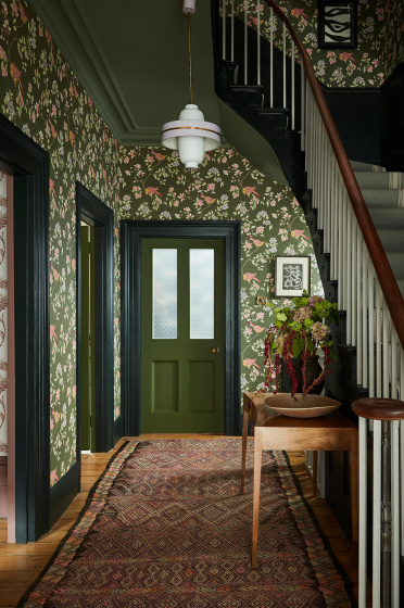 High ceiling hallway featuring dark green floral wallpaper (Aderyn - Olive Colour) with dark green woodwork and a tapestry rug.