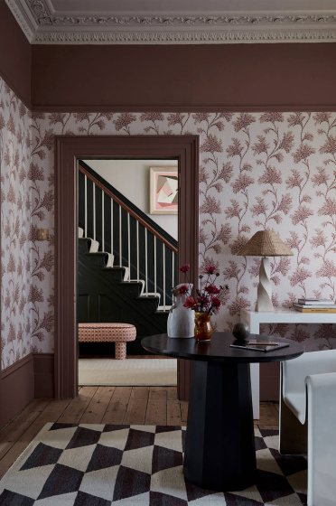 Living space featuring pink floral wallpaper (Mosaic Trail - Blush) with a dark table and chair with a door leading out to a staircase.